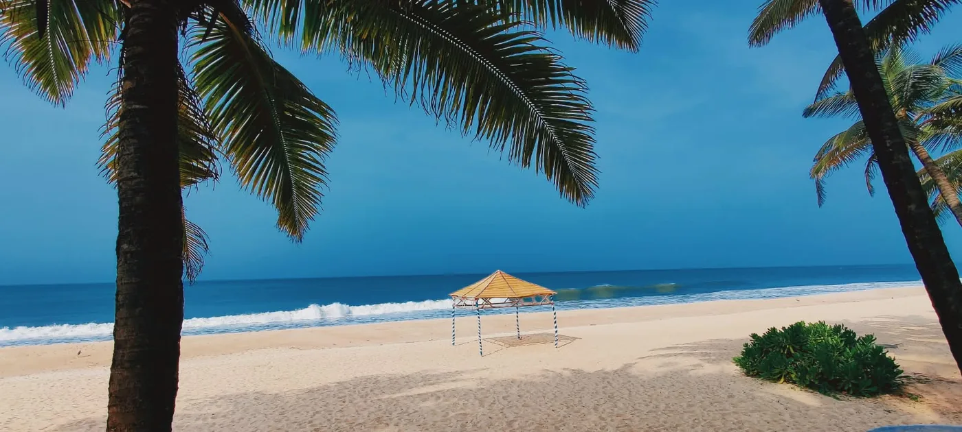 A beach hut on white sand, framed by two leaning palm trees